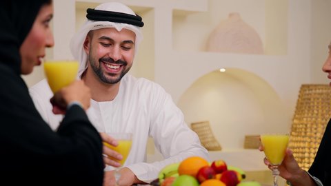 عائلة عربية خليجية إماراتية تجلس معًا حول طاولة ، يتبادلون الفواكه الطازجة ، شرب عصير البرتقال، جلسة ضيافة تقليدية ، لحظات ودية مليئة بالمحبة والانسجام، أجواء عائلية دافئة ، الاستمتاع بتناول المشروبات الباردة
