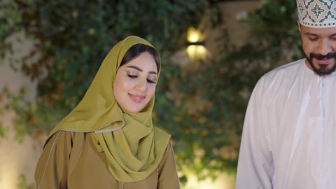 Fun activities and events, cooperation and participation in preparing food, chatting and exchanging conversations between spouses with gestures of integration, a close-up of an Omani Gulf Arab woman wearing an abaya participating with her husband in the process of grilling food, outings and entertainment in a high-end tourist chalet during the holiday