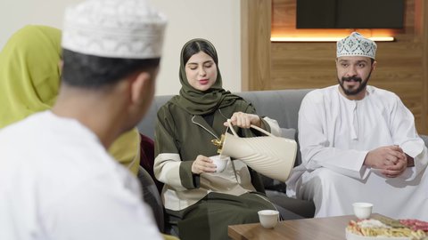 اجتماع الأهل والأصدقاء في الهواء الطلق، قضاء وقت ممتع ومسلي مع مجموعة من الأصدقاء، أصدقاء عربيون خليجيون عمانيون بالزي التقليدي يشربون القهوة العربية ويتبادلون الأحاديث والقصص بإيماءات الاندماج، التنزه والتسلية والترفيه في شاليه سياحية في عمان