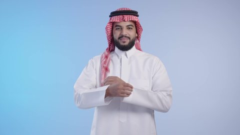 الوقوف باستقامة وثقه بالنفس، الاهتمام بالمظهر الخارجي، مفهوم الاناقه و الرجولة، شاب وسيم عربي خليجي سعودي مسرور يرتدي الشماغ والثوب التقليدي ينظر إلى الكاميرا بإيماءات أيدي متقاطعه