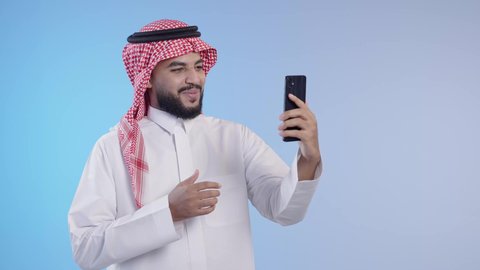 التواصل مع الأصدقاء والأقارب عبر التطبيقات والتقنيات الحديثة والمتطورة, الاشارة بعلامة اللايك,  رجل عربي خليجي سعودي مبتسم يرتدي الثوب التقليدي والشماغ يستخدم الهاتف المحمول