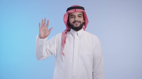 النظر الى الكاميرا بايماءات السعادة والسرور، مفهوم الاستقبال والترحيب, التعارف و الصداقه وتكوين علاقات, إلقاء التحيه والسلام, رجل عربي خليجي سعودي يرتدي الثوب التقليدي والشماغ يقوم برفع يده للتلويح لشخص ما