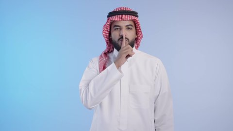 لتوقف عن الكلام وخفض الصوت، الهدوء والسكون وعدم الإزعاج, اشارات طلب السكوت والصمت، رجل عربي خليجي سعودي يرتدي الشماغ والثوب التقليدي ويضع أصبع السبابة على فمه بإيماءات وجه غاضبة