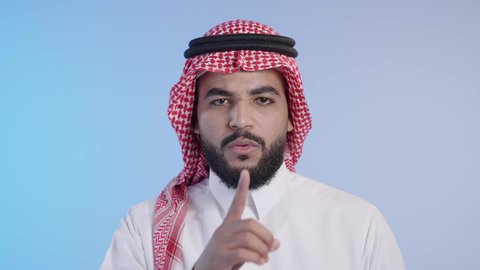 اشارات طلب السكوت والصمت، رجل عربي خليجي سعودي يرتدي الشماغ والثوب التقليدي ويضع أصبع السبابة على فمه بإيماءات وجه غاضبة، التوقف عن الكلام وخفض الصوت، الهدوء والسكون وعدم الإزعاج