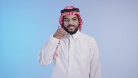 إشارة تعني إتصل بي, تعابير الفرح والسرور، انتظار مكالمة وإستخدام الميكروفون، رجل عربي خليجي سعودي مبتسم يرتدي الثوب التقليدي والشماغ يرفع يده بإيماءات الإتصال