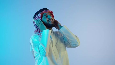 الاستمتاع بتقنية الهيدفون، رجل عربي خليجي سعودي مبتسم يرتدي الثوب التقليدي و الشماغ و يستخدم الجوال والأجهزة التكنولوجية, قضاء أوقات ممتعة ومسلية