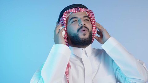 قضاء أوقات ممتعة ومسلية, الاستمتاع بتقنية الهيدفون، رجل عربي خليجي سعودي مبتسم يرتدي الثوب التقليدي و الشماغ و يستخدم الجوال والأجهزة التكنولوجية