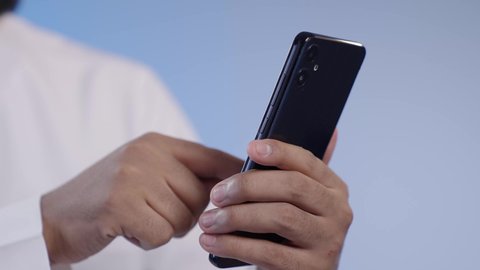 النقر على شاشة الجوال, استخدام الأجهزة التقنية الحديثة و المتطورة, رجل عربي خليجي سعودي مبتسم يرتدي الثوب التقليدي يمسك الهاتف المحمول بيده