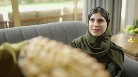 تبادل الاحاديث والدردشات، زيارات وتجمعات عائليه, اكرام الضيف وحسن الاستقبال ، تصوير مقرب لسيدة عربية خليجية عمانية محجبة ترتدي العباءة تقوم بتناول الحلويات العربية