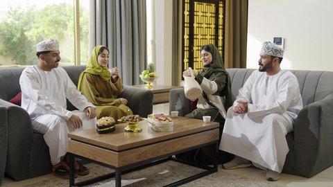 التنزه والتسلية والترفيه في شاليه سياحية في عمان، كرم الاستقبال والضيافة، اجتماع الأهل والأصدقاء، قضاء وقت ممتع ومسلي مع الاقارب، عائلة عرب خليجيون عمانيون بالزي التقليدي يشربون القهوة العربية ويتبادلون الأحاديث بإيماءات الاندماج