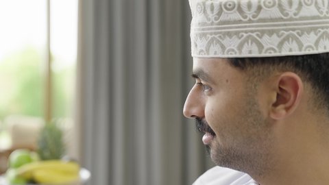 ايماءات السعادة والسرور، الانصات وسماع سوالف سعيده، تصوير مقرب لرجل عربي خليجي عماني يرتدي الدشداشة والكمة  يجلس على اريكه يقوم بالتحدث مع شخص ما، تبادل الاخبار والاحاديث