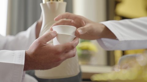 مفهوم حسن الضيافة والكرم، تصوير مقرب ليد رجل عربي خليجي عماني يرتدي الدشداشة يقوم بصب القهوة العربية الساخنة في الفنجان، تبادل الاخبار والاحاديث