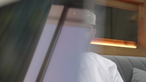 جهاز تقني حديث ومتطور، تصفح الانترنت ومواقع السوشال ميديا، تعابير السعادة والسرور، إنجاز مهام العمل عن بعد عبر الجوال ، تصوير مقرب لشاب عربي خليجي عماني مثقف يرتدي الدشداشة والكمة يجلس في إحدى الشاليهات يقوم باستخدام الهاتف المحمول
