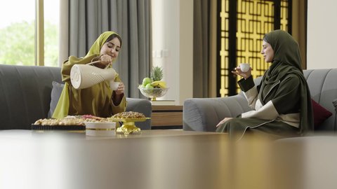 تناول القهوة والحلويات، حسن الضيافة والكرم، بناء علاقات اجتماعية ناجحة، النقاشات والحوارات في الأجواء الهادئة، سيدتان عمانيتان تقضيان اوقات ممتعة في إحدى الشاليهات، امرأة عربية خليجية سعودية ترتدي الحجاب والعباءة تجلس على الأريكة مع صديقتها بإيماءات السعادة