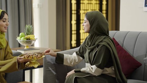 حسن الضيافة والكرم، بناء علاقات اجتماعية ناجحة، النقاشات والحوارات في الأجواء الهادئة، سيدتان عمانيتان تقضيان اوقات ممتعة في إحدى الشاليهات، امرأة عربية خليجية سعودية ترتدي الحجاب والعباءة تجلس على الأريكة مع صديقتها بإيماءات السعادة، تناول القهوة والحلويات