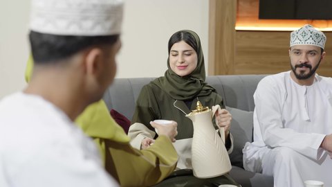 أسرة عربية خليجية عمانيه يرتدون الذي التقليدي يجلسون في غرفه المعيشه في جلسه وناسه، مشاركة الاحاديث والاخبار بين الافراد, الزيارات والاجتماعات العائليه، حسن الاستقبال والضيافه الاصيله