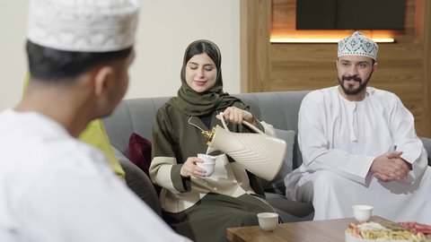 Sharing conversations and news between individuals, an Omani Gulf Arab family wearing traditional clothes sitting in the living room in a pleasant atmosphere, family visits and gatherings, good reception and authentic hospitality
