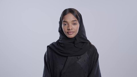 مفهوم الأنوثه والنعومه, الاهتمام بالمظهر الخارجي,  الوقوف باسقامة وثقه بالنفس,بورتريه لطالبة جامعية سمراء عربيه سعوديه ترتدي العباءه والحجاب تنظر إلى الكاميرا بإيماءات السعادة و السرور, خلفية بيضاء