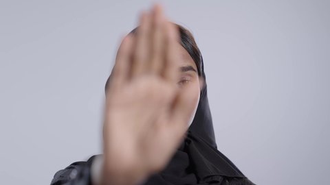 طلب الامتناع عن الاقتراب, حماية النفس من ضرر خارجي, طالبة جامعية سمراء عربيه سعوديه ترتدي العباءه والحجاب  تنظر إلى الكاميرا و ترفع يدها بتعابير التوقف عن شيء ما، الاشارة بعدم الموافقة, خلفية بيضاء