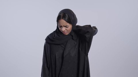 آلام الرقبة والعظام والعمود الفقري، إيماءات الوجه تدل على الاضطراب والتألم، ضرورة الذهاب للطبيب والحصول على العلاج،بورتريه لطالبة جامعية سمراء عربيه سعوديه ترتدي العباءه والحجاب تمسك رقبتها بإيماءات الألم, خلفية بيضاء