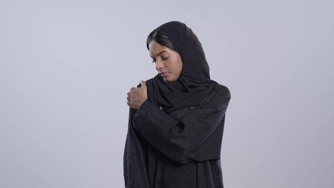 إيماءات الألم في الأكتاف، التهاب العضلات والمفاصل، الإحساس بالتعب والإرهاق, بورتريه لطالبة جامعية سمراء عربيه سعوديه ترتدي العباءه والحجاب تضع يدها على كتفها بتعابير الوجع، الحاجه لوضع خطة علاجية, خلفية بيضاء
