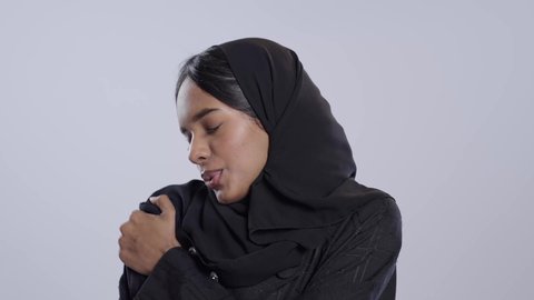 التهاب العضلات والمفاصل، الإحساس بالتعب والإرهاق, إيماءات الألم في الأكتاف، بورتريه لطالبة جامعية سمراء عربيه سعوديه ترتدي العباءه والحجاب تضع يدها على كتفها بتعابير الوجع، الحاجه لوضع خطة علاجية, خلفية بيضاء