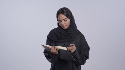 قضاء وقت الفراغ بالتثقيف والتعلم، مفهوم محو الأمية، التزود بالعلم والمعرفة، طالبة جامعية سمراء عربيه سعوديه ترتدي العباءه والحجاب تمارس هواية مطالعة الكتب المفيدة في وقت الفراغ، القراءه بإيماءات التمعن والتركيز