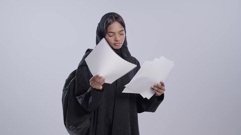 اعداد التقارير الخاصة ، طالبة جامعية سمراء عربيه سعوديه ترتدي العباءه والحجاب تحمل بيدها مجموعة من الاوراق،  مراجعة ومتابعة الخطط والمشاريع الدراسيه، التدقيق في قراءة الملاحظات، خلفية بيضاء