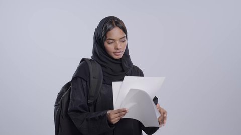 طالبة جامعية سمراء عربيه سعوديه ترتدي العباءه والحجاب تحمل بيدها مجموعة من الاوراق،  مراجعة ومتابعة الخطط والمشاريع الدراسيه، اعداد التقارير الخاصة بالعمل، التدقيق في قراءة الملاحظات، خلفية بيضاء