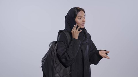 الدردشة والتحدث مع الأصدقاء، تصفح مواقع وتطبيقات الانترنت، اجراء مكالمه هاتفيه ، طالبة جامعية سمراء عربيه سعوديه ترتدي العباءه والحجاب وشنطه سوداء تمسك الجوال بيدها، استخدام التقنيات والتكنولوجيا الحديثة بالحياة اليومية ، خلفيه بيضاء