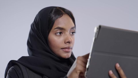 الدردشة والتحدث مع الأصدقاء، تصفح مواقع وتطبيقات الانترنت، اجراء مكالمه فيديو، طالبة جامعية سمراء عربيه سعوديه ترتدي العباءه والحجاب  تمسك جهاز التابلت بيدها، استخدام التقنيات والتكنولوجيا الحديثة بالحياة اليومية ، خلفيه بيضاء