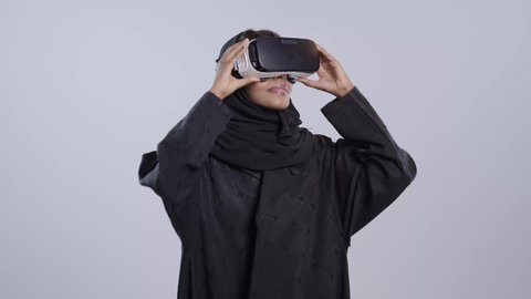المتعة والتسلية بالمشاهدة عبر نظارة الواقع الافتراضي, طالبة جامعية سمراء عربيه سعوديه ترتدي العباءه والحجاب تضع نظارات ثلاثية الأبعاد تقوم برفع كف يدها للاعلى بتعابير الاندماج , ايماءات التوقف عن فعل امر ما