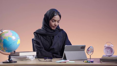 دمج التقنيات الحديثة بالمجال التعليمي ، استخدام التكنولوجيا الحديثة في الأعمال الدراسيه ،التعامل مع المنصات الاونلاين فى التعليم عن بعد، بورتريه لطالبة جامعية سمراء عربيه سعوديه ترتدي العباءه والحجاب  تجلس على مكتب وتستخدم جهاز التابلت