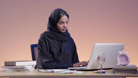 استخدام التكنولوجيا الحديثة في الأعمال الدراسيه ، دمج التقنيات الحديثة بالمجال التعليمي ،التعامل مع المنصات الاونلاين فى التعليم عن بعد، بورتريه لطالبة جامعية سمراء عربيه سعوديه ترتدي العباءه والحجاب  تجلس على مكتب وتستخدم جهاز اللابتوب