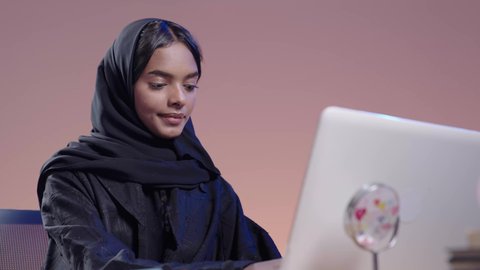 Interacting with online platforms in distance learning. Portrait of a black female Saudi Arabian university student wearing an abaya and hijab sitting at a desk using a laptop. Integrating modern technologies in the educational field. Using modern technology in academic work.