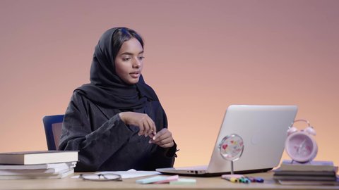 اجراء مكالمه فيديو ،التعامل مع جهاز الحاسوب المحمول فى التعليم عن بعد، بورتريه لطالبة جامعية سمراء عربيه سعوديه ترتدي العباءه والحجاب  تجلس على مكتب وتستخدم جهاز اللابتوب  ، استخدام التكنولوجيا الحديثة في الأعمال الدراسيه، دمج التقنيات الحديثة بالمجال التعليمي