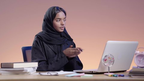 Working with a laptop in distance learning. Portrait of a black female Saudi Arabian university student wearing an abaya, hijab sitting at a desk using a laptop. Using modern technology in academic work. Integrating modern technologies into the educational field.