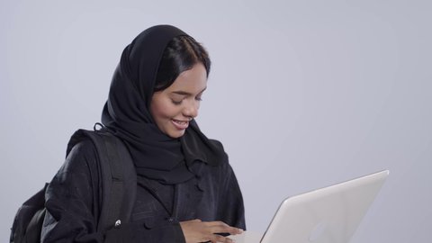 Using modern technology in academic work, integrating advanced technologies into the educational field. Portrait of a black, Arab, Saudi university student wearing an abaya and hijab, holding a laptop.