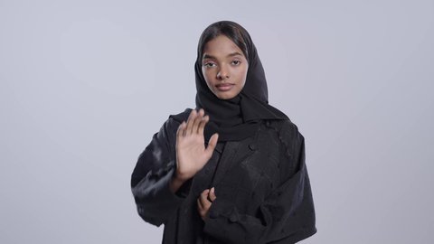 طلب الامتناع عن الاقتراب, حماية النفس من ضرر خارجي, طالبة جامعية سمراء عربيه سعوديه ترتدي العباءه والحجاب  تنظر إلى الكاميرا و ترفع يدها بتعابير التوقف عن شيء ما، الاشارة بعدم الموافقة, خلفية بيضاء