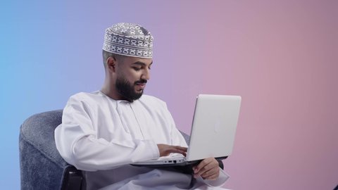 استخدام الأجهزة والتقنيات الحديثة المتطورة، اجتماع عمل عبر الإنترنت، رجل عربي خليجي عماني يرتدي الدشداشه والكمه يقوم بإجراء مكالمة فيديو عبر جهاز اللابتوب ، اداره  شؤون الأعمال وتنظيمها عن بعد