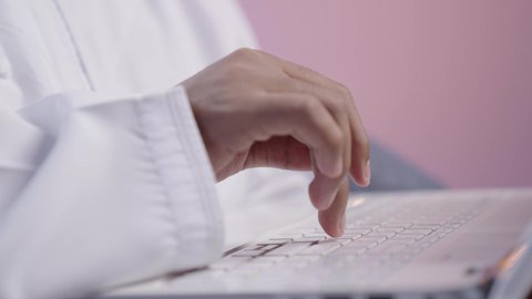 اجتماع عمل عبر الإنترنت، استخدام الأجهزة والتقنيات الحديثة المتطورة، تصوير مقرب ليد رجل عربي خليجي عماني يرتدي الدشداشه والكمه يقوم بإجراء مكالمة فيديو عبر جهاز اللابتوب ، اداره  شؤون الأعمال وتنظيمها عن بعد