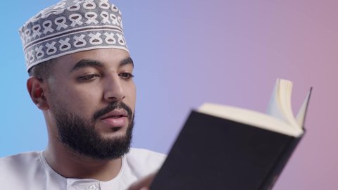 Gaining knowledge and information, spending free time educating and learning, the concept of literacy, an Omani Gulf Arab man wearing a dishdasha and a kuma practicing his hobby of reading useful books in his free time, reading with gestures of contemplation and concentration.