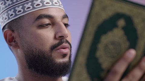 Reciting and reading the Holy Quran and contemplating its meanings. An Arab Gulf Omani man wearing a dishdasha and a keema holding the Holy Quran. Frequent remembrance of God Almighty, feeling humbleness and tranquility. Colorful background.