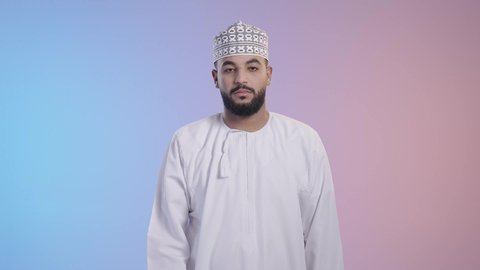 الاشارة بعدم الموافقة, حماية النفس من ضرر خارجي,  طلب الامتناع عن الاقتراب, شاب عربي خليجي عماني يرتدي الدشداشه والكمه ، ينظر إلى الكاميرا و يرفع يده بتعابير التوقف عن شيء ما، خلفية ملونة