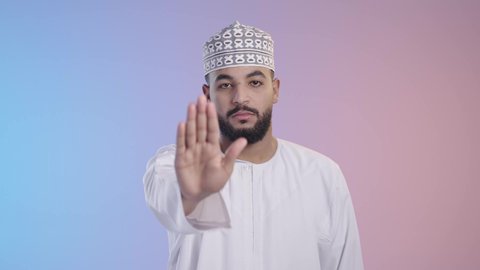 حماية النفس من ضرر خارجي,  طلب الامتناع عن الاقتراب, شاب عربي خليجي عماني يرتدي الدشداشه والكمه ، ينظر إلى الكاميرا و يرفع يده بتعابير التوقف عن شيء ما، الاشارة بعدم الموافقة, خلفية ملونة