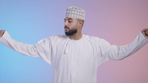 اللياقة البدنية والجسم الصحي المتين، التمتع بالبنية الجسدية القوية، شاب عربي خليجي عماني يرتدي الدشداشه والكمه ويقوم بعرض عضلات يديه، إيماءات وجه ويدين تدل على القوة العضلية، خلفية ملونة