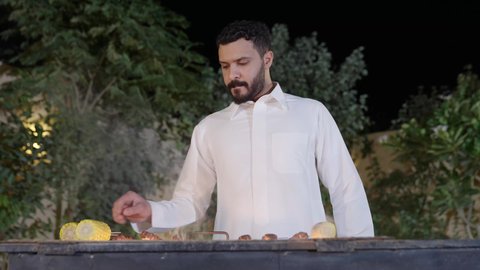 تحضير الشواء في التجمعات، فعاليات وأنشطة مسلية، التعاون والمشاركة في تحضير الطعام، ولد عربي خليجي سعودي يرتدي الزي الكاجوال ويقوم بعملية الشواء تقليب اللحم على الموقد التأكد من طهيه جيدا، التنزه والتسلية في شاليه سياحي راقي وقت العطلة