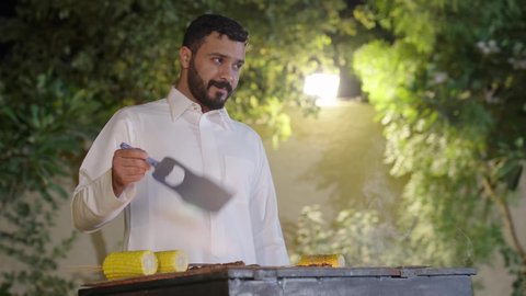 التعاون والمشاركة في تحضير الطعام، التنزه والتسلية في شاليه سياحي راقي وقت العطلة ،فعاليات وأنشطة مسلية، تحضير الشواء في التجمعات،ولد عربي خليجي سعودي يرتدي الزي الكاجوال ويقوم بعملية الشواء تقليب اللحم على الموقد التأكد من طهيه جيدا