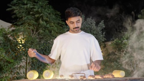 Excursion and entertainment in a luxury chalet during the holiday, cooperation and participation in preparing food, entertaining events and activities, preparing barbecue in gatherings, a close-up of a Saudi Arabian Gulf boy wearing casual clothes and performing the barbecue, turning the meat on the stove to ensure it is cooked well