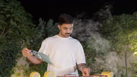 التعاون والمشاركة في تحضير الطعام، فعاليات وأنشطة مسلية،  تحضير الشواء في التجمعات، تصوير مقرب لولد عربي خليجي سعودي يرتدي الزي الكاجوال ويقوم بعملية الشواء تقليب اللحم على الموقد التأكد من طهيه جيدا، التنزه والتسلية في شاليه سياحي راقي وقت العطلة